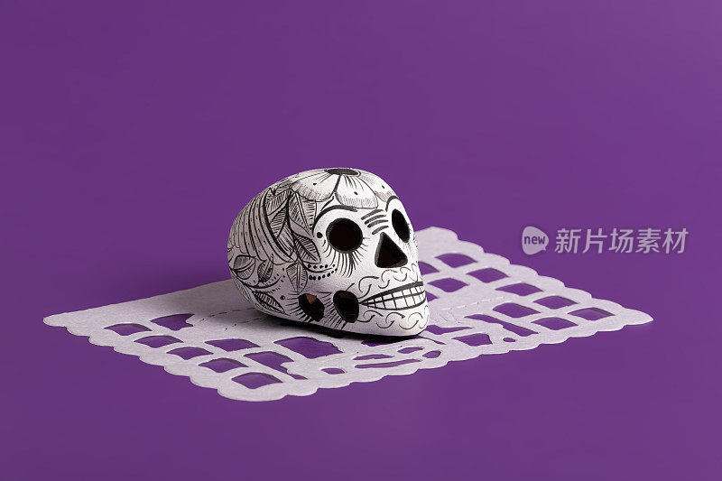 死亡的一天的陶器头骨(calavera)在黑色papel picado在紫色背景，Dia de Muertos背景